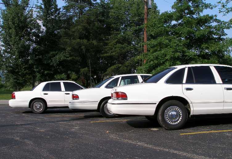 Three white Ford Crown Victorias parked in a lot, side view