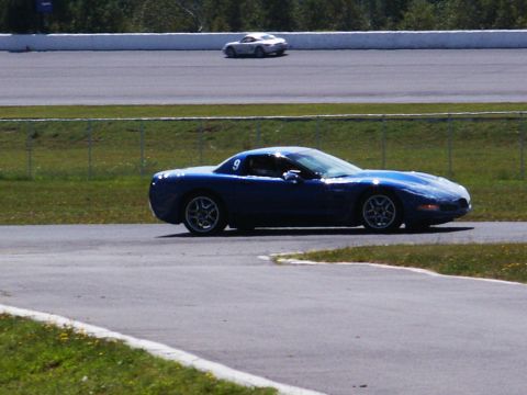 2001 Mercury Grand Marquis - A blue sports car navigates a turn on a race track, with another vehicle visible in the distance.
