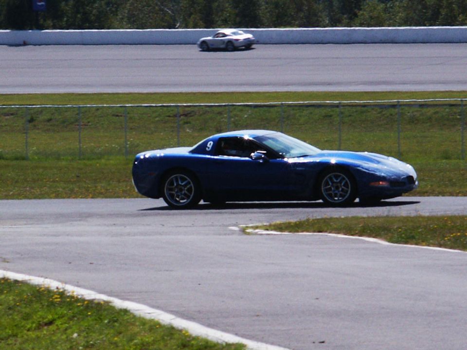 Blue sports car on a race track, number 9 on door. Another white car in the background