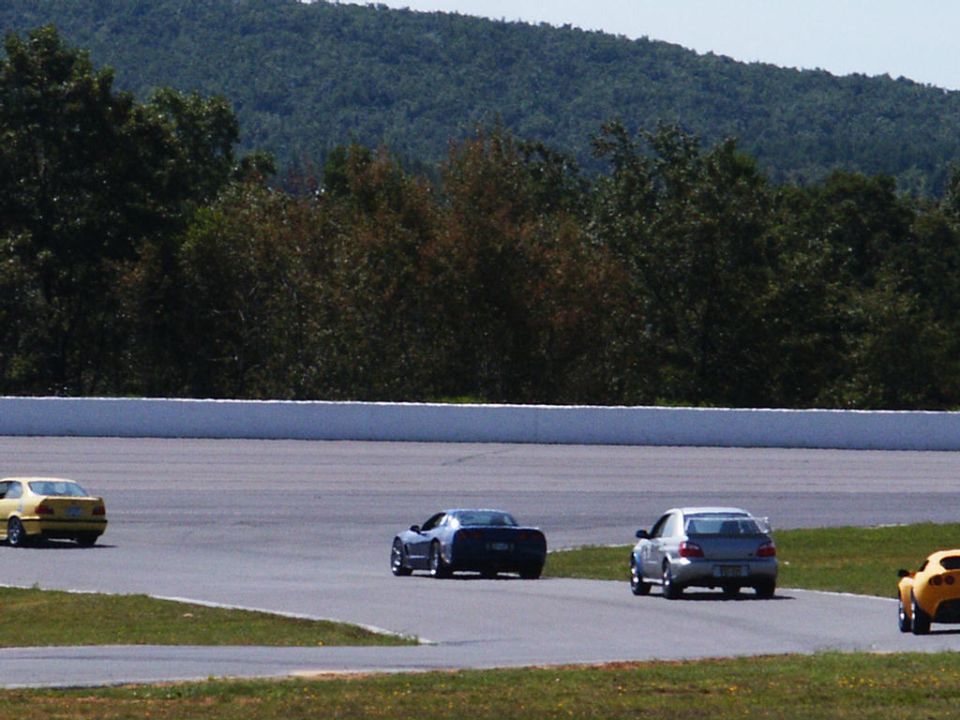 Several cars are on a race track with trees and a hill in the background