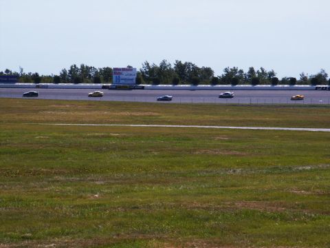 2001 Mercury Grand Marquis - Cars compete on a sunny day at the racetrack, with a large billboard visible in the distance.