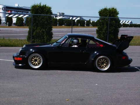 2001 Mercury Grand Marquis - A black Porsche 911 Turbo is parked on asphalt with a racetrack and trees in the background.