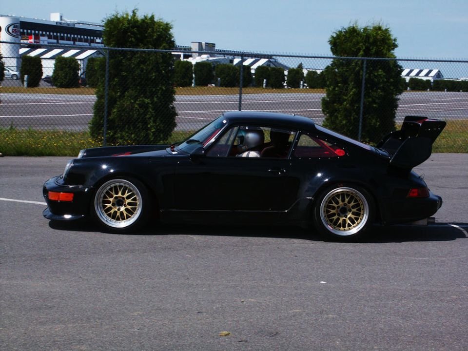 Black Porsche 911 Turbo with gold BBS wheels and a prominent rear wing, seen from the side