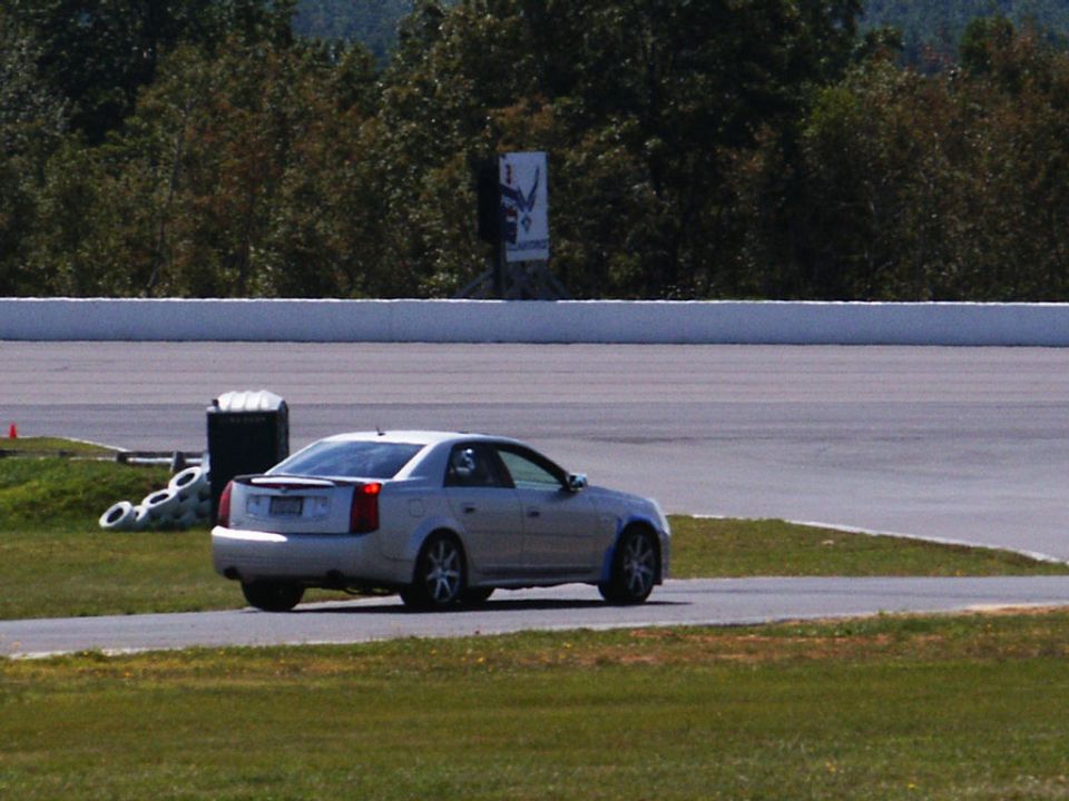 Silver sedan on race track, rear view. Supermotors.net logo visible