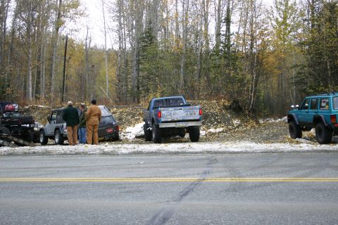 2003 Jeep TJ - Multiple off-road vehicles are parked on the side of a road with trees in the background.