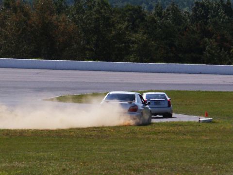 2001 Mercury Grand Marquis - Two cars are on a racetrack, with one kicking up a cloud of dust as it turns.