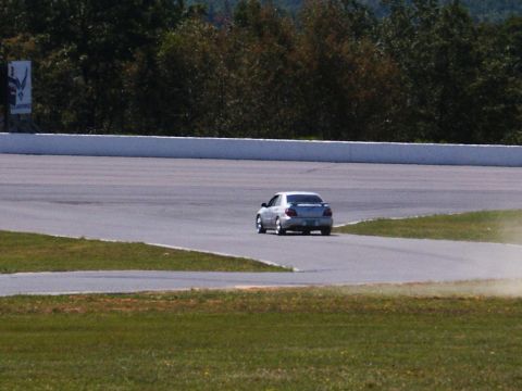 2001 Mercury Grand Marquis - A silver sedan navigates a turn on a race track, kicking up a bit of dust.
