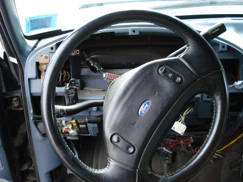 1994 Ford Bronco - The interior of a Ford vehicle shows a steering wheel with exposed wiring and a blue sticker on the windshield.