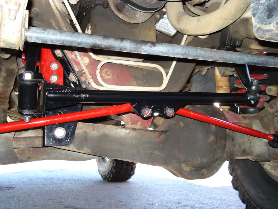 Undercarriage view of red and black suspension parts, including a sway bar and linkage, attached to a vehicle's differential and frame