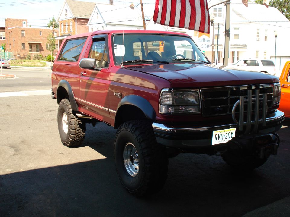 Red 1994 Ford Bronco with large tires and custom grille guard