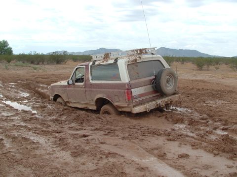 1990 Ford Bronco - A maroon and white Ford Bronco is stuck deep in mud after driving off-road.