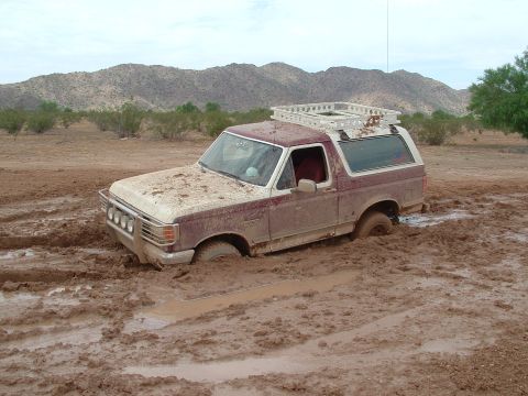 1990 Ford Bronco - A maroon and white Ford Bronco is stuck deep in mud with its front end submerged.