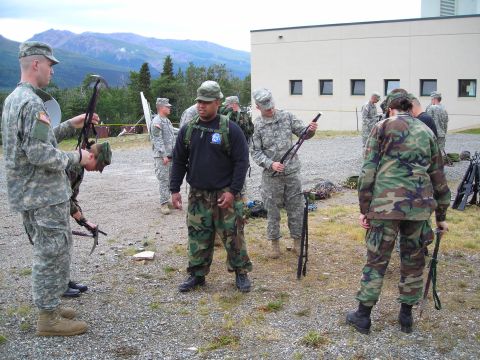 2003 Jeep TJ - Military personnel are gathered outdoors, handling rifles and equipment near a building.
