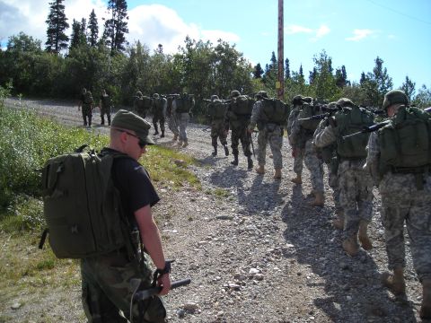 2003 Jeep TJ - A group of soldiers with backpacks and rifles walk in formation on a dirt path under a bright sky.