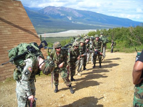 2003 Jeep TJ - A group of soldiers carrying gear and rifles on a training exercise with mountainous terrain behind them.