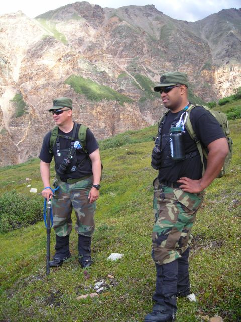 2003 Jeep TJ - Two men in camouflage gear stand in a grassy mountain landscape, looking out at the terrain.