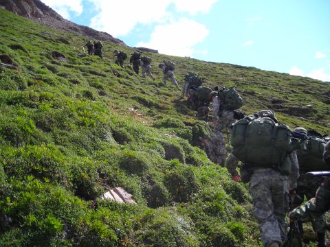 2003 Jeep TJ - A group of soldiers in camouflage gear trek up a , grassy slope, carrying heavy backpacks.