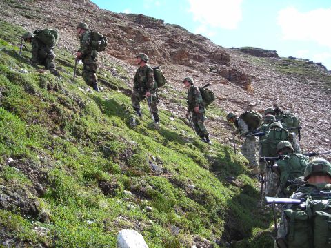 2003 Jeep TJ - A group of soldiers navigates a challenging, uneven terrain on a sunny day.