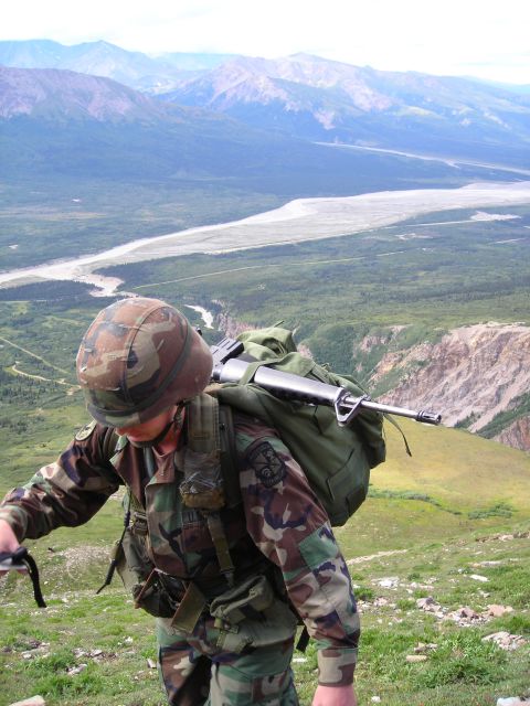 2003 Jeep TJ - Soldier with rifle and backpack traverses a mountain landscape with a river valley below.