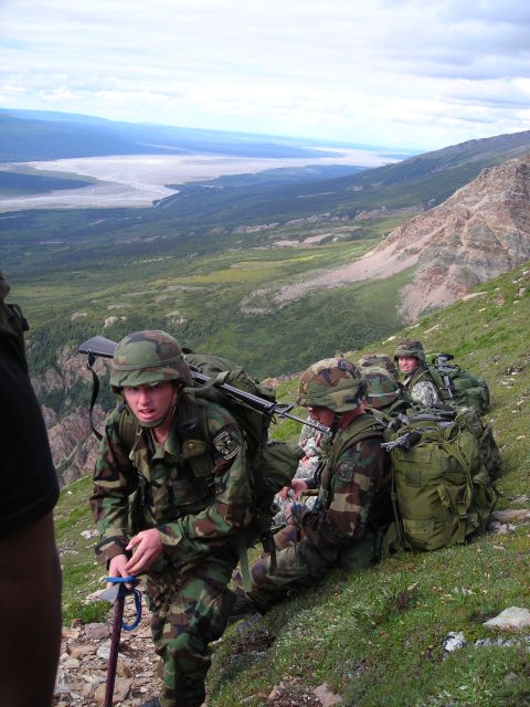 2003 Jeep TJ - A group of soldiers with heavy packs navigate a steep, grassy mountainside with a vast valley below.