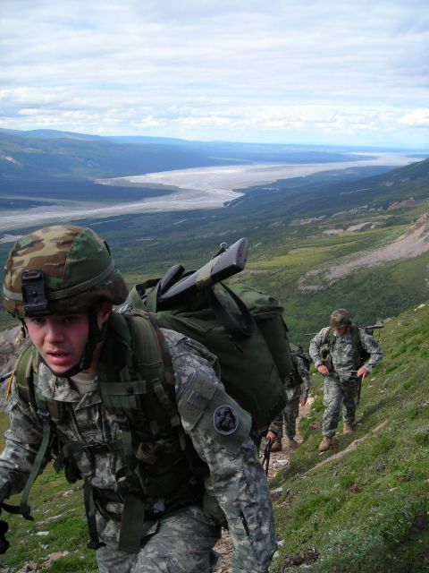 2003 Jeep TJ - A group of soldiers ascend a mountain path, carrying gear and rifles, with a vast river valley stretching out below.