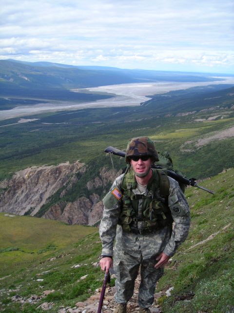 2003 Jeep TJ - A soldier traverses a mountain trail with a rifle and backpack, surveying a vast valley below.