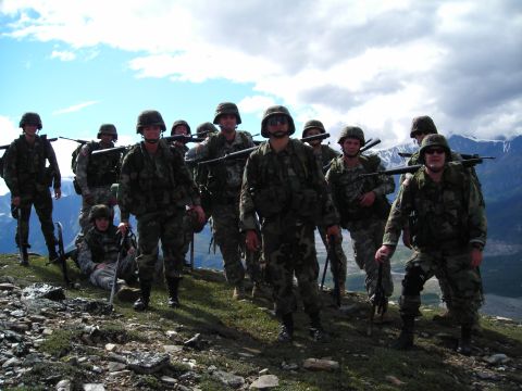 2003 Jeep TJ - A group of soldiers stand on a mountainside, equipped with rifles and gear, under a cloudy sky.