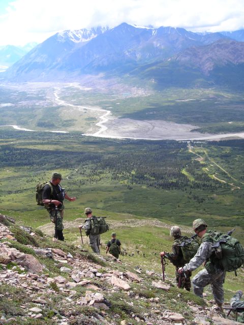 2003 Jeep TJ - A group of soldiers navigates a steep, rocky mountain trail, with a vast valley and distant mountains stretching out behind them.