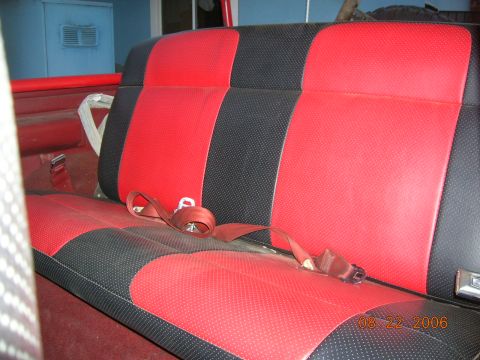 1985 Ford Bronco - Interior view of a vehicle's rear seat with red and black upholstery and a seatbelt.