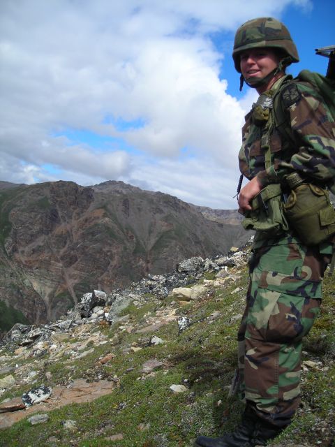 2003 Jeep TJ - A soldier in camouflage stands on a rocky slope overlooking a mountainous landscape under a cloudy sky.