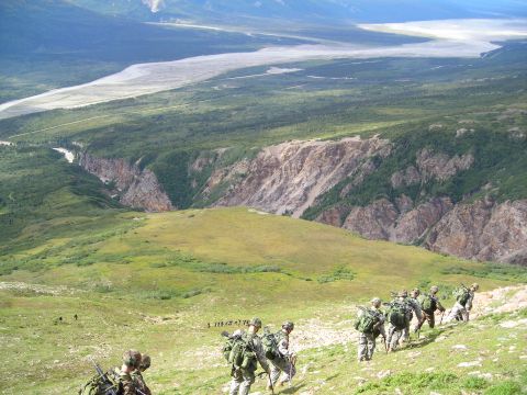 2003 Jeep TJ - Soldiers traverse a steep, grassy mountain slope overlooking a wide river valley and distant mountains.