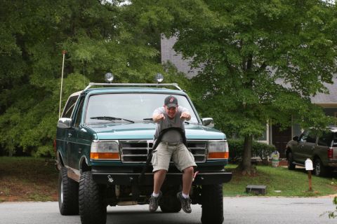 1990 Ford Bronco - A man sits on the hood of a green Ford Bronco, which appears to be a 1992 model, with another vehicle visible in the background.