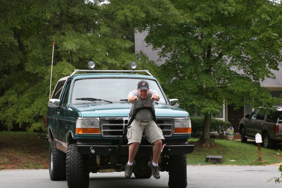 Green Ford Bronco with a man sitting on the hood, front view. The grille and headlights suggest a 1992 model year