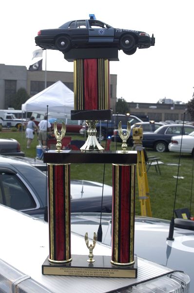 1978 Dodge Monaco - A trophy a toy police car is displayed, with other vehicles visible in the background at an outdoor event.