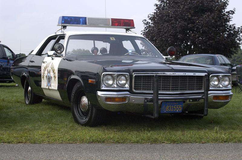 Black and white police car with "Highway Patrol" on door, parked on grass