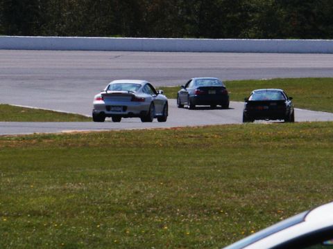 2001 Mercury Grand Marquis - Three cars are on a racetrack, with a silver Porsche leading the pack.
