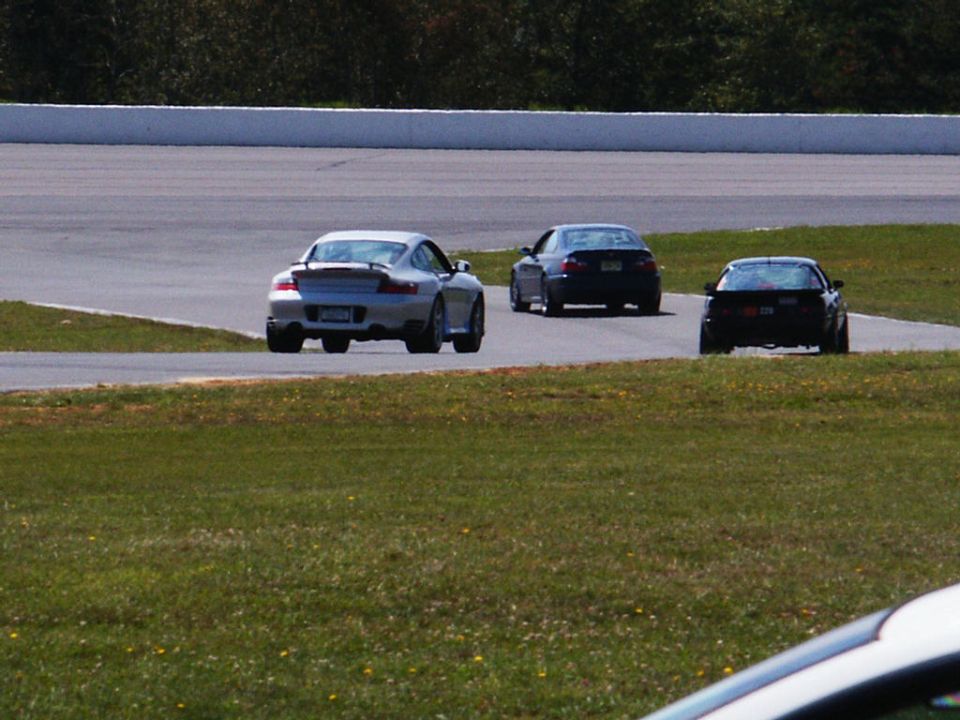 Silver Porsche 911, dark sedan, and black coupe driving on a racetrack