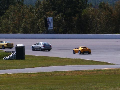 2001 Mercury Grand Marquis - Three sports cars race on a track with trees and a sign in the background.