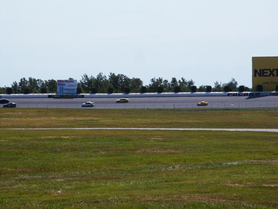 Several race cars on a track with trees and a large yellow sign in the background