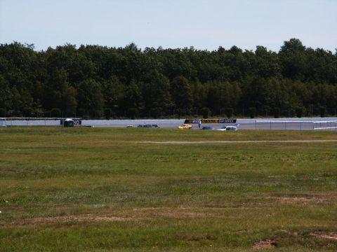 2001 Mercury Grand Marquis - Multiple vehicles race on a track, with a wooded area and fence lining the course.