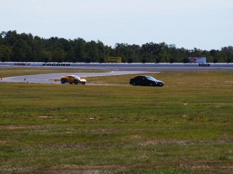 2001 Mercury Grand Marquis - Two cars are on the track at Pocono Raceway, with trees and a bright sky overhead.