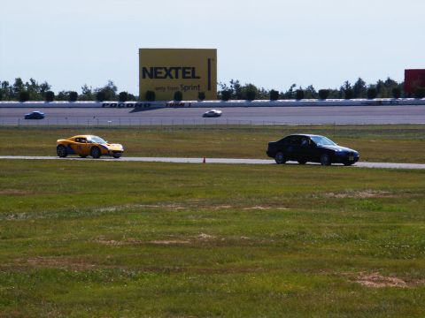 2001 Mercury Grand Marquis - Multiple vehicles race on a track under a bright sky, with a prominent advertising billboard visible.