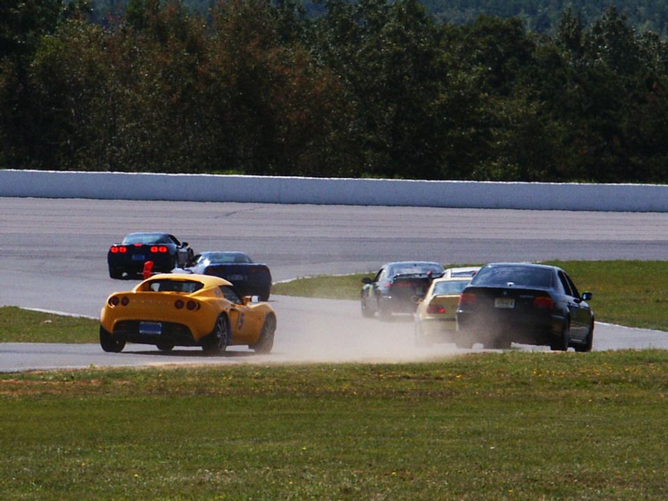 Several cars racing on a track, kicking up dust