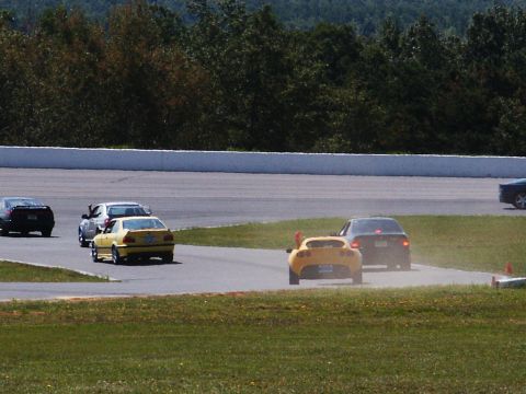 2001 Mercury Grand Marquis - Several cars are competing on a race track with trees and a white barrier in the background.