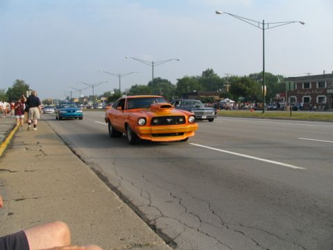 1978 Ford Mustang II - Orange Mustang II Cobra hatchback with black hood scoop, front air dam and dark side stripes cruising toward the camera in the right lane o…