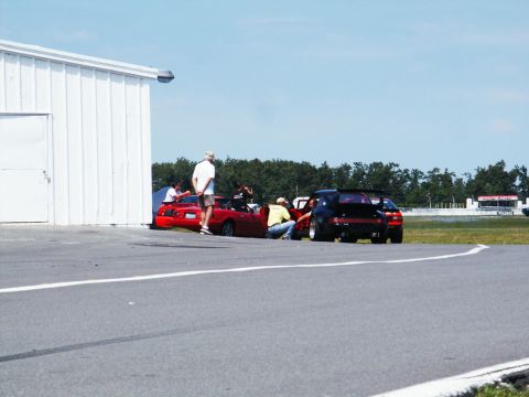 2001 Mercury Grand Marquis - People are interacting with sports cars on a paved area, possibly a racetrack, with a building and trees in the background.