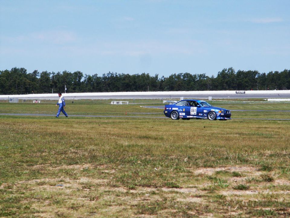 Blue coupe with racing decals and number 061 on a grassy track
