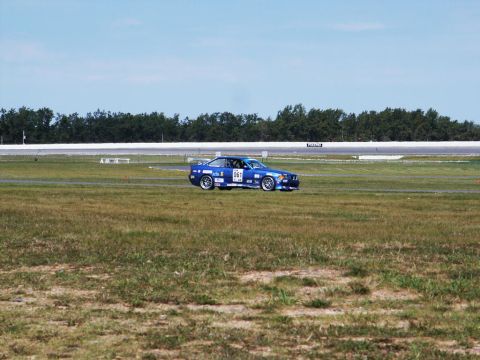 2001 Mercury Grand Marquis - A blue race car with the number 061 visible on its door is seen on a grassy area next to a race track.