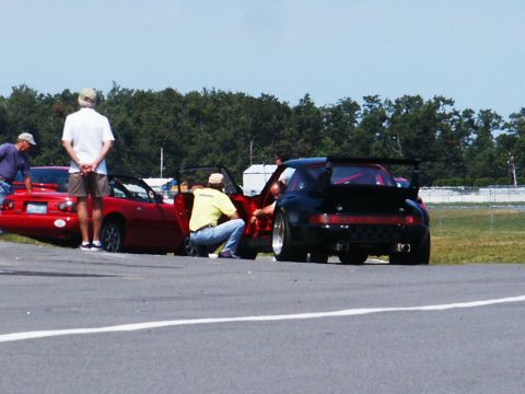 2001 Mercury Grand Marquis - A black Porsche 911 is parked on a track next to a red convertible with people around.