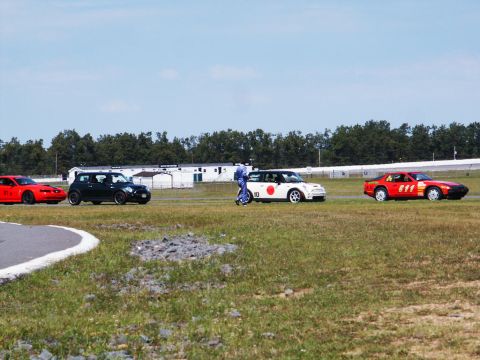 2001 Mercury Grand Marquis - Several cars are lined up on a grassy area next to a racetrack under a clear blue sky.